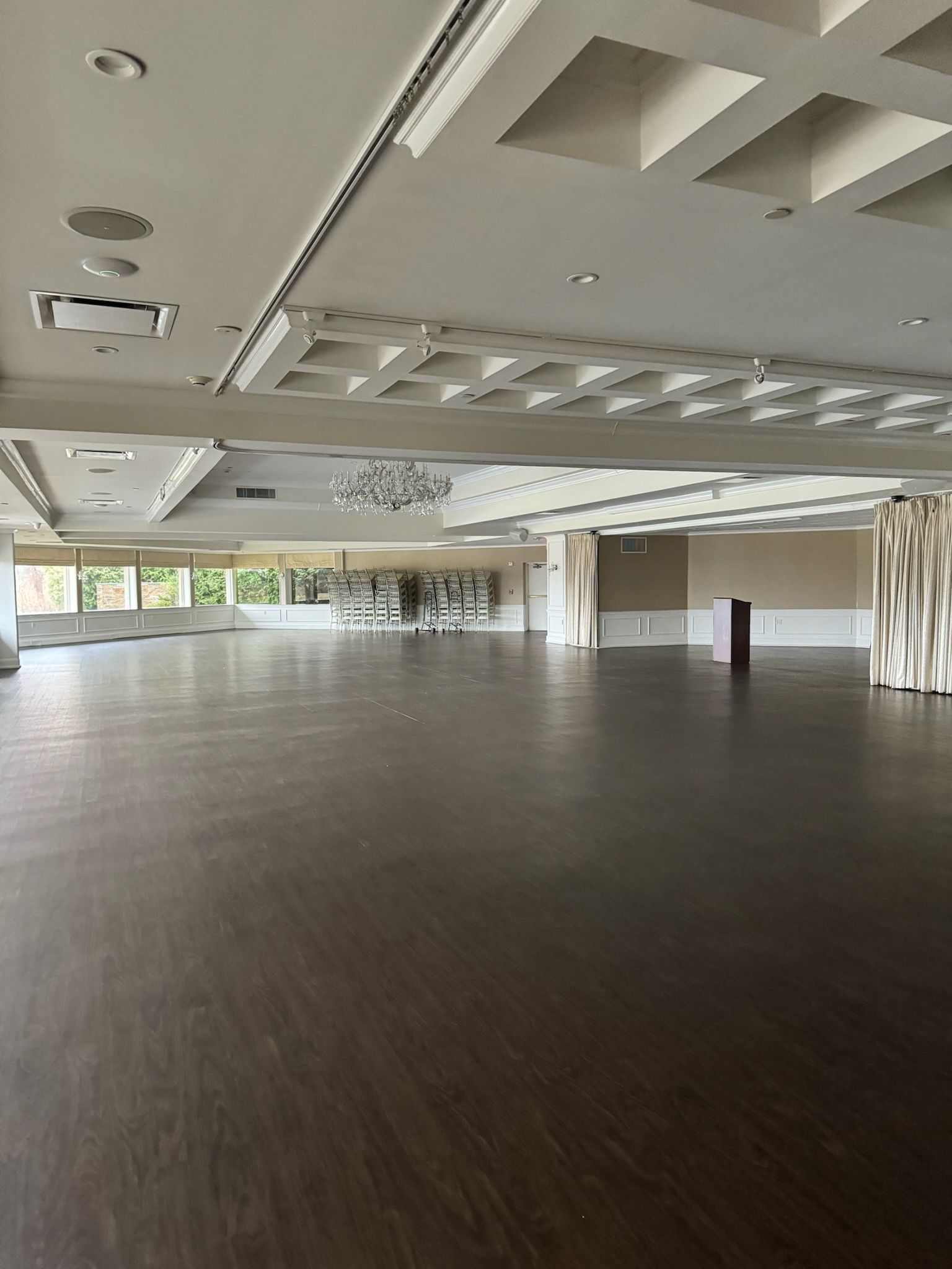 Empty modern conference hall with dark wood floor, recessed ceiling lights, and large windows along one side