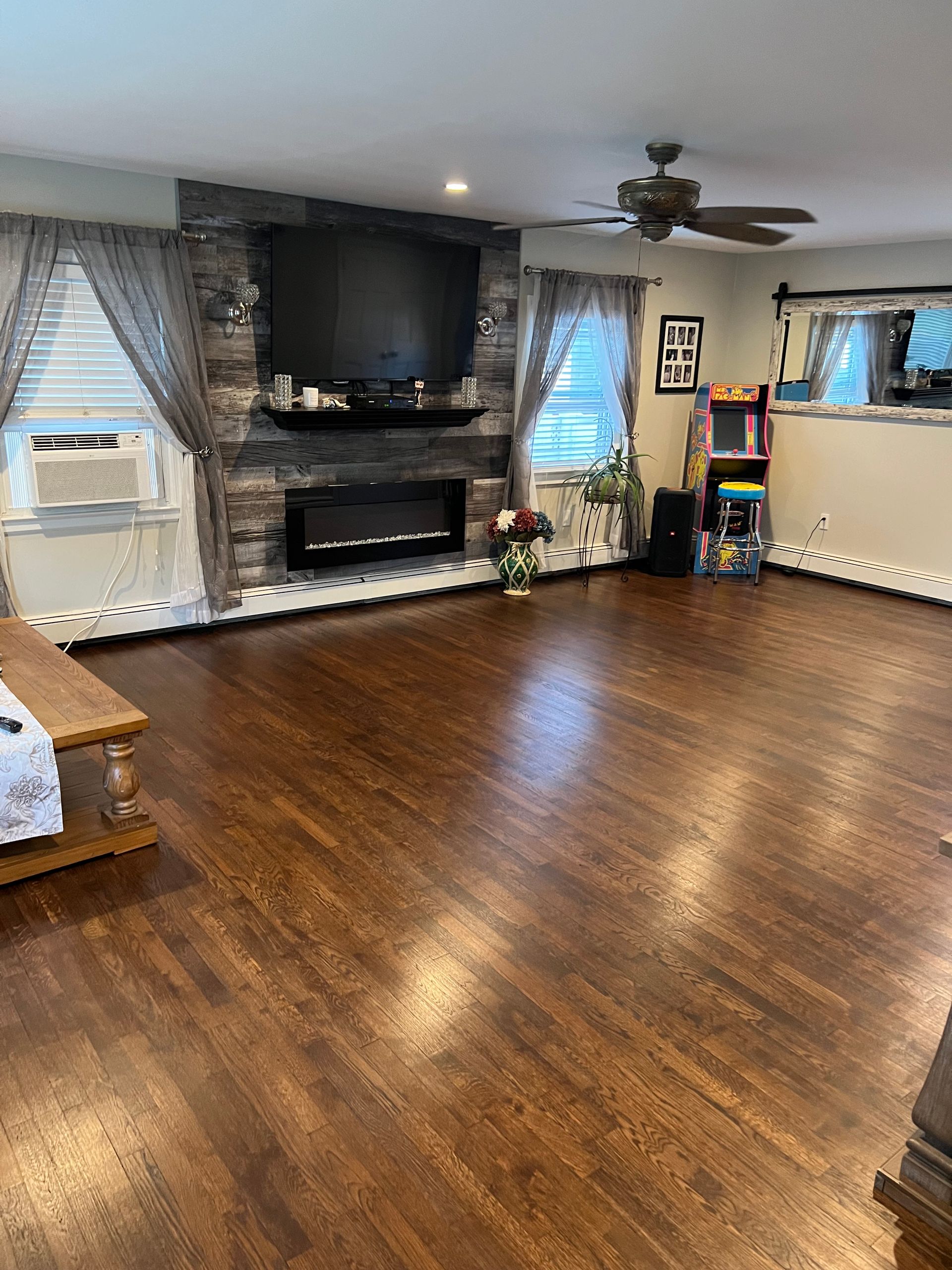 Spacious living room with wood floors, fireplace, TV, ceiling fan, and windows with sheer curtains