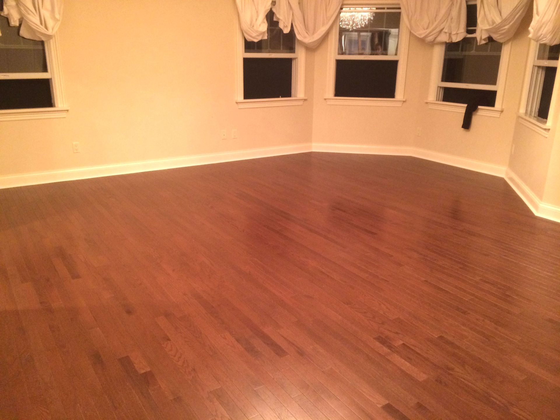 Empty room with hardwood floors, beige walls, and bay windows with curtains