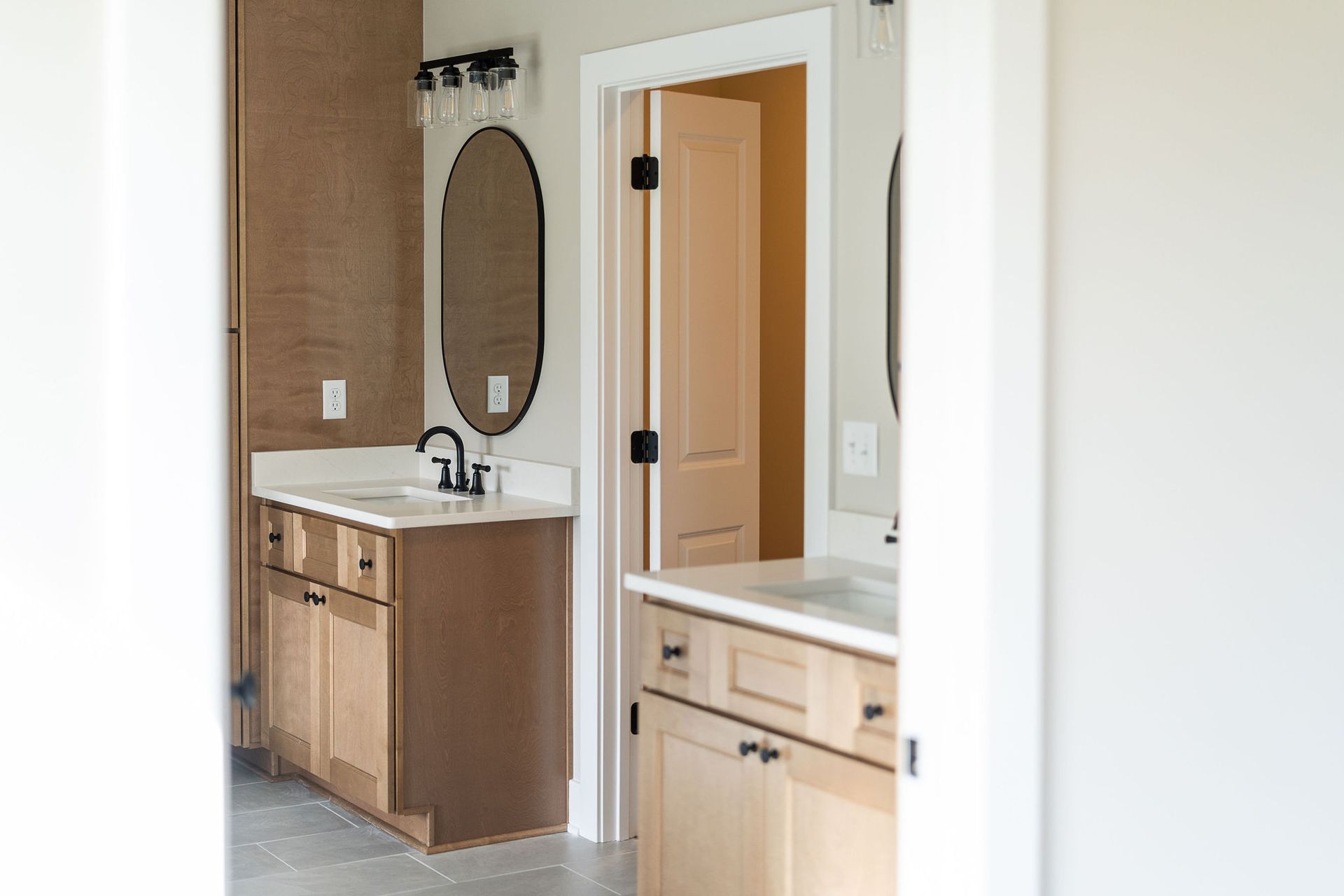 Bathroom with two vanities, oval mirrors, and a door.
