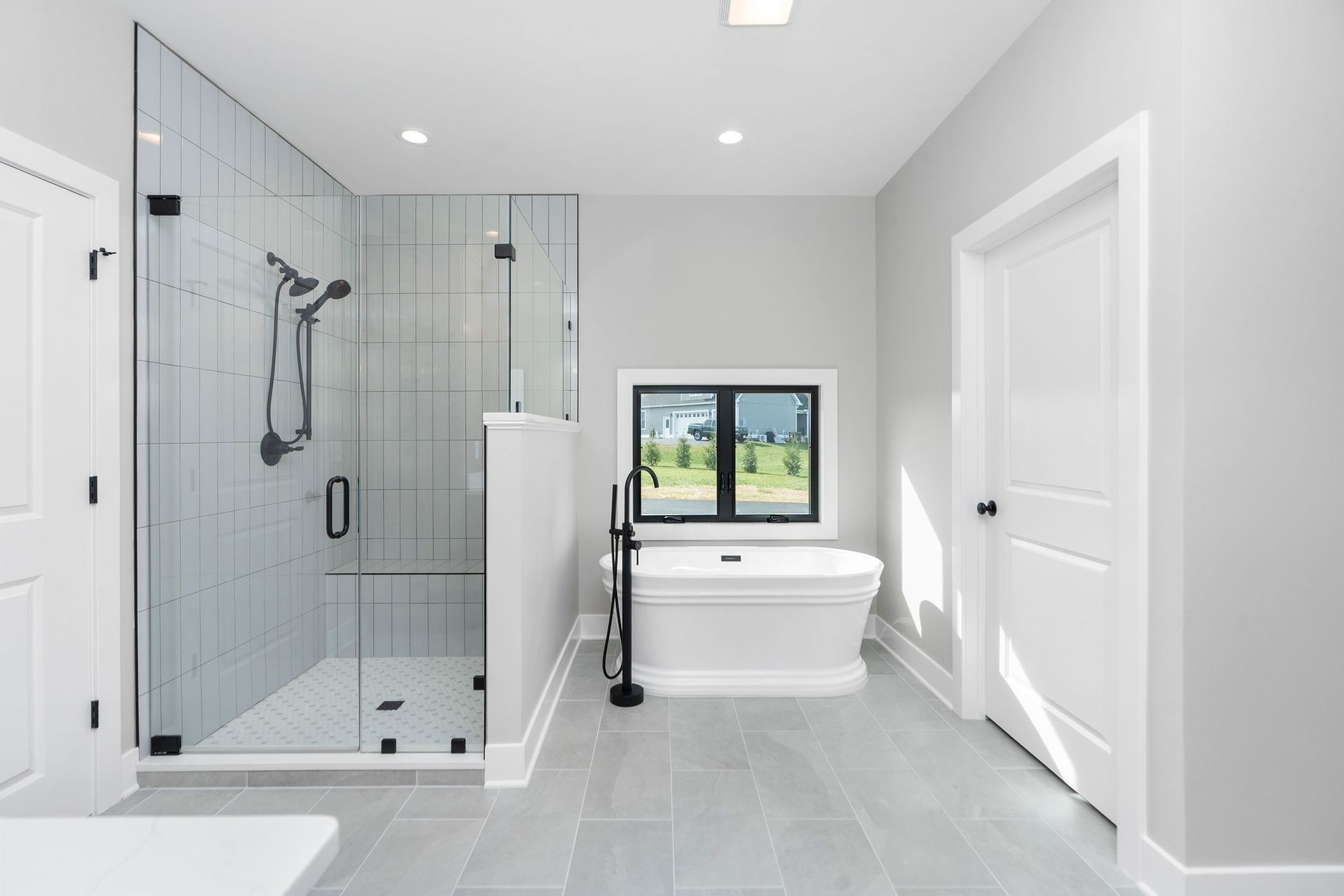 Modern, light gray bathroom with walk-in shower, freestanding tub, and small window.