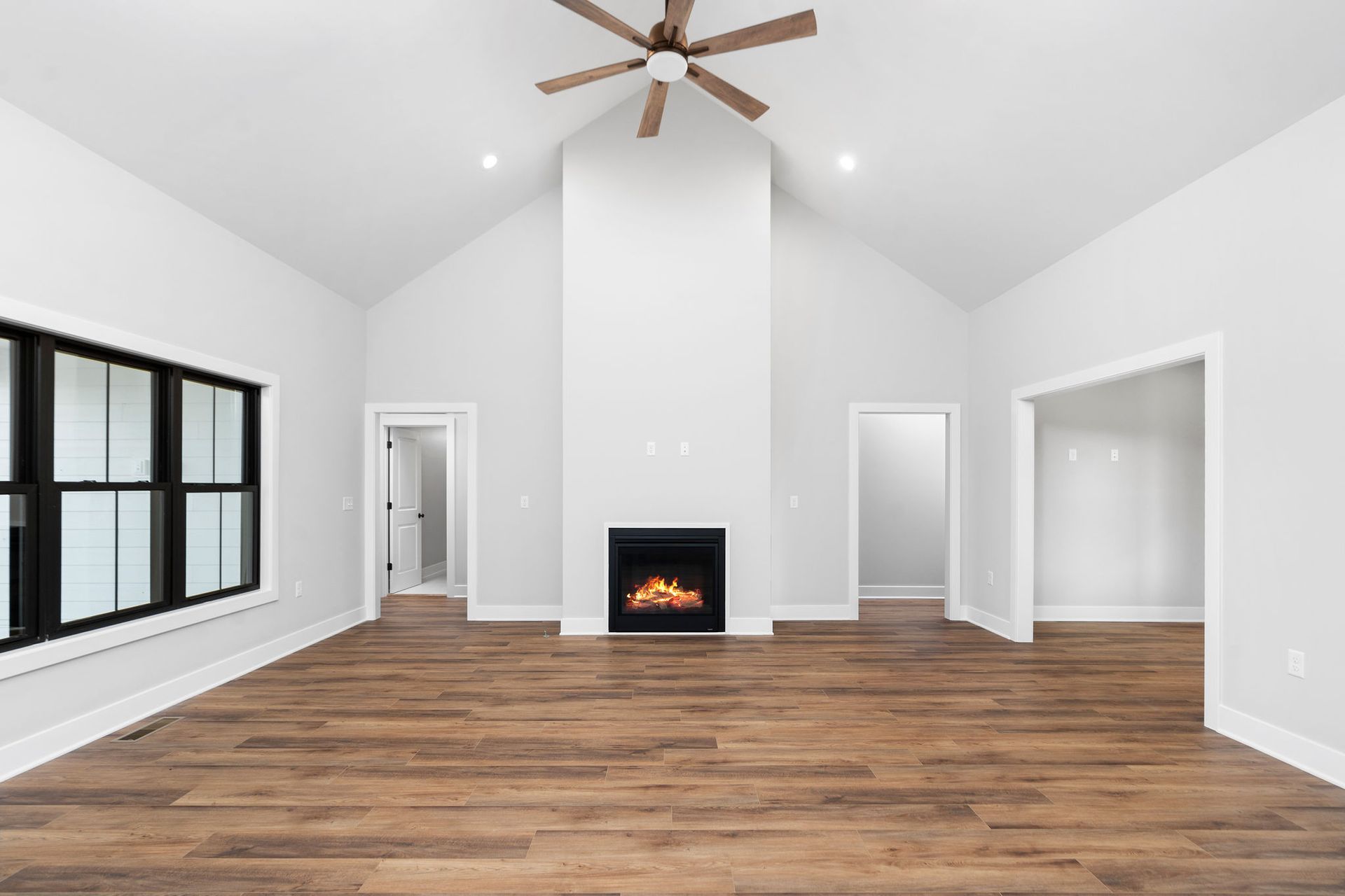 Empty living room with vaulted ceiling, fireplace, and wood-look flooring.