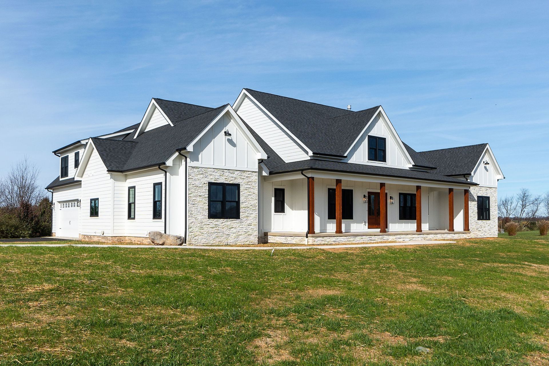 White farmhouse with black roof and windows, wooden porch columns, on a green lawn.