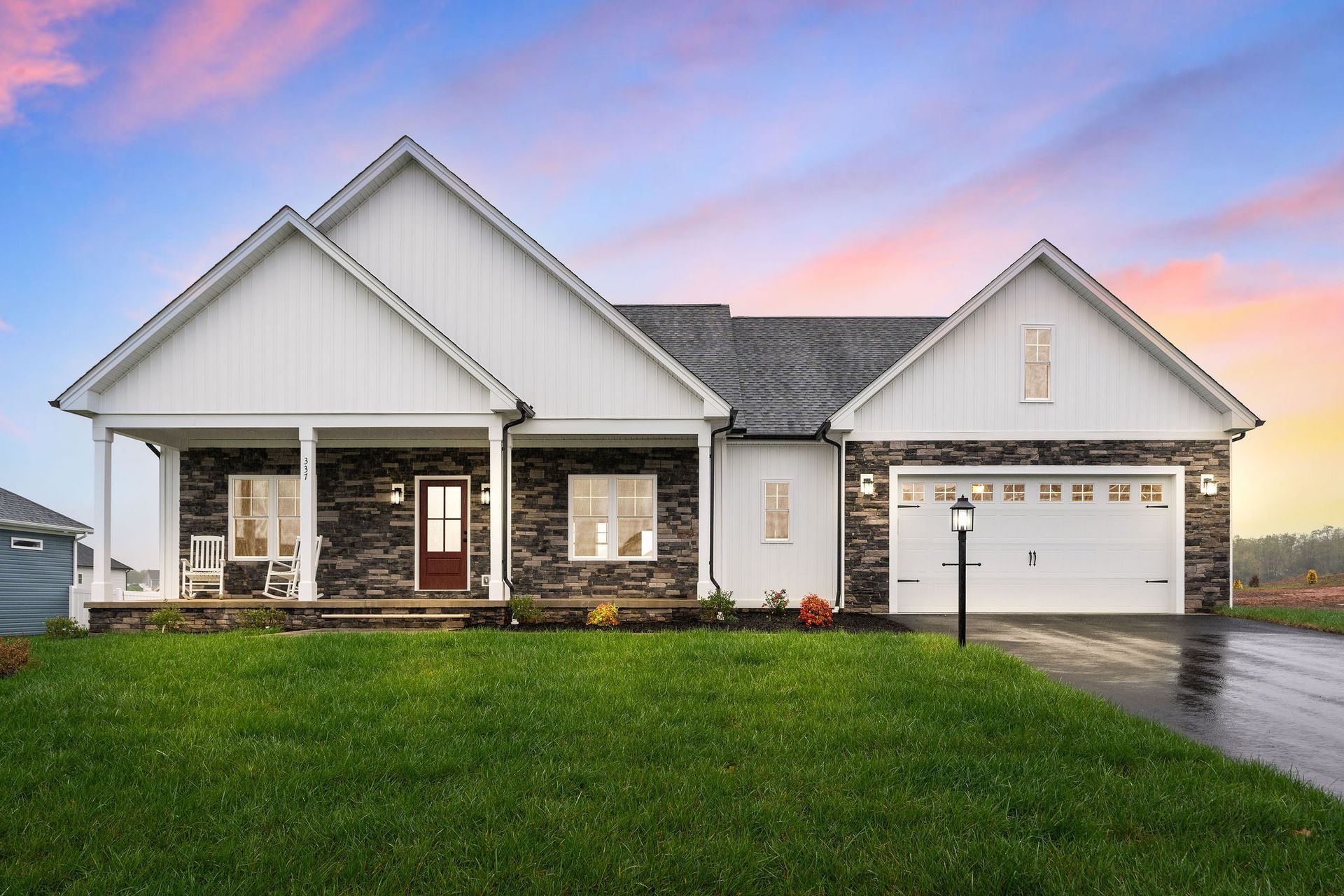 Ranch-style house with stone and white siding, front porch, and attached garage under a colorful sunset.