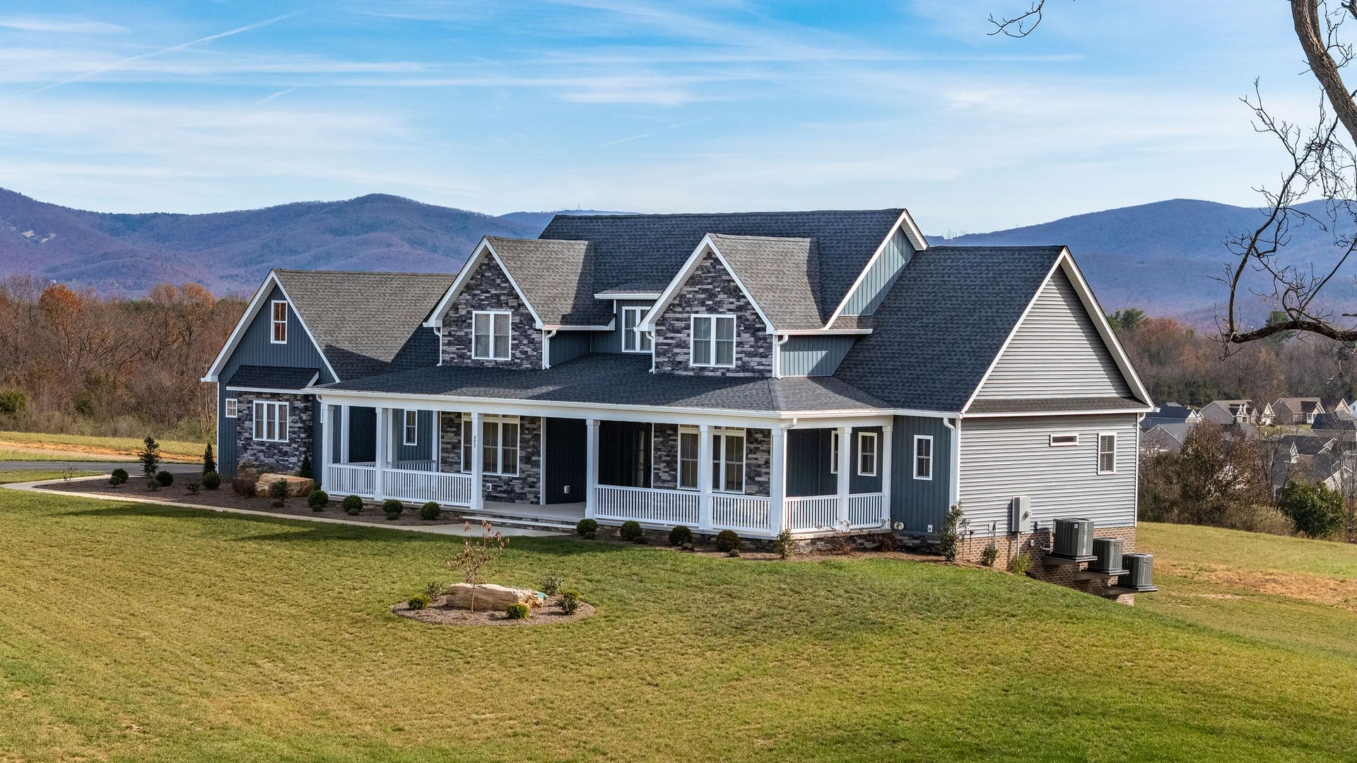 Blue house with a wraparound porch, set against mountains and a blue sky.