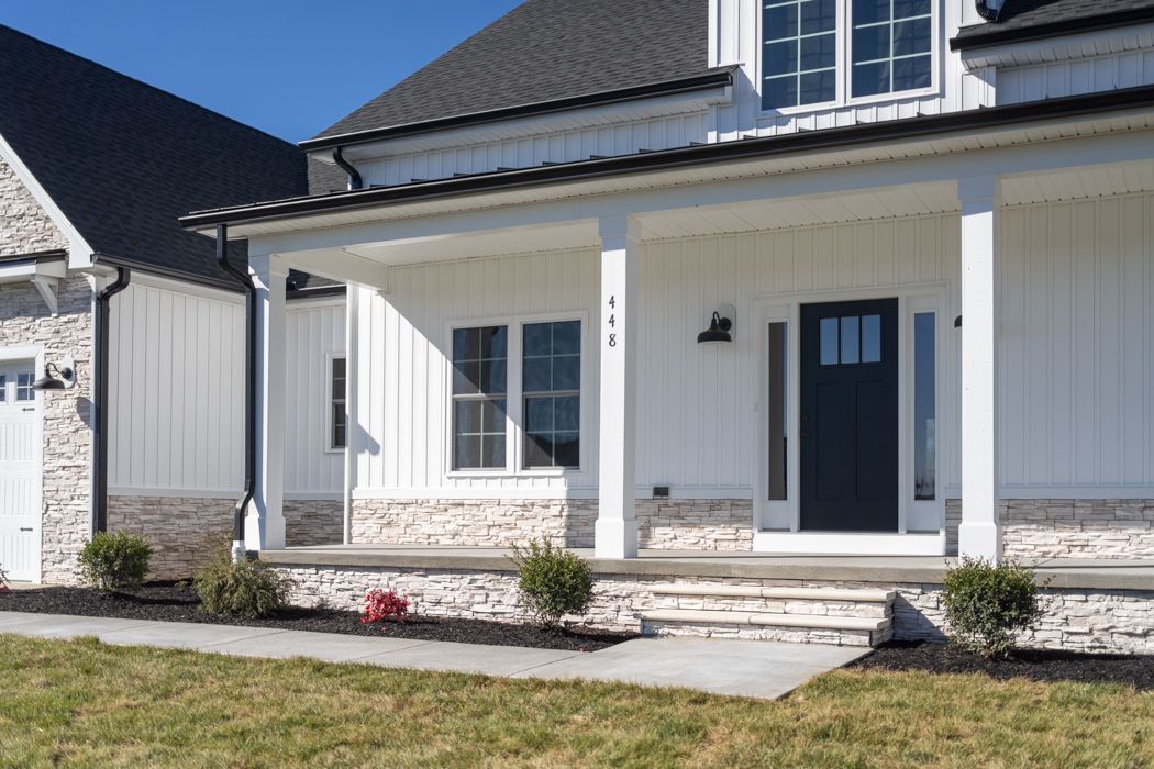 White farmhouse exterior with stone base, front porch, and black door.