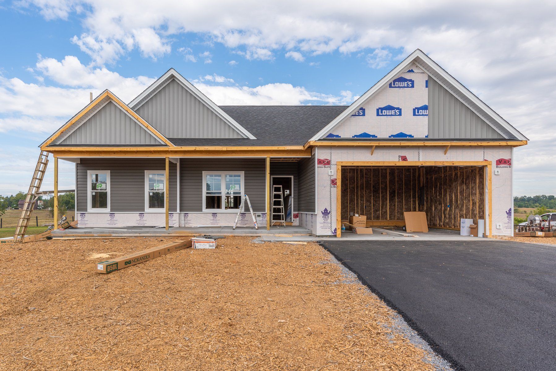New house under construction with gray siding, open garage, and blue sky.