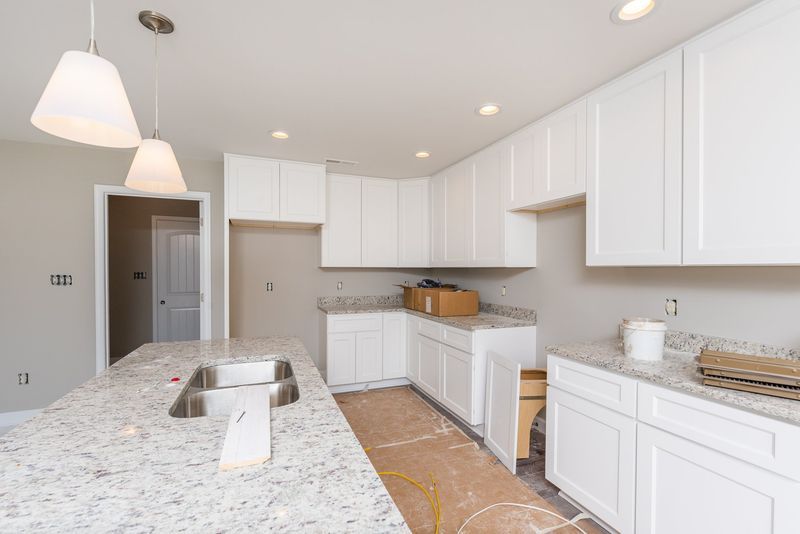 White kitchen with granite countertops, cabinets, and island. Unfinished with light fixtures.