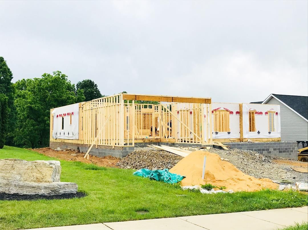 A house under construction. Wooden frame on a concrete foundation, surrounded by construction materials, overcast sky.
