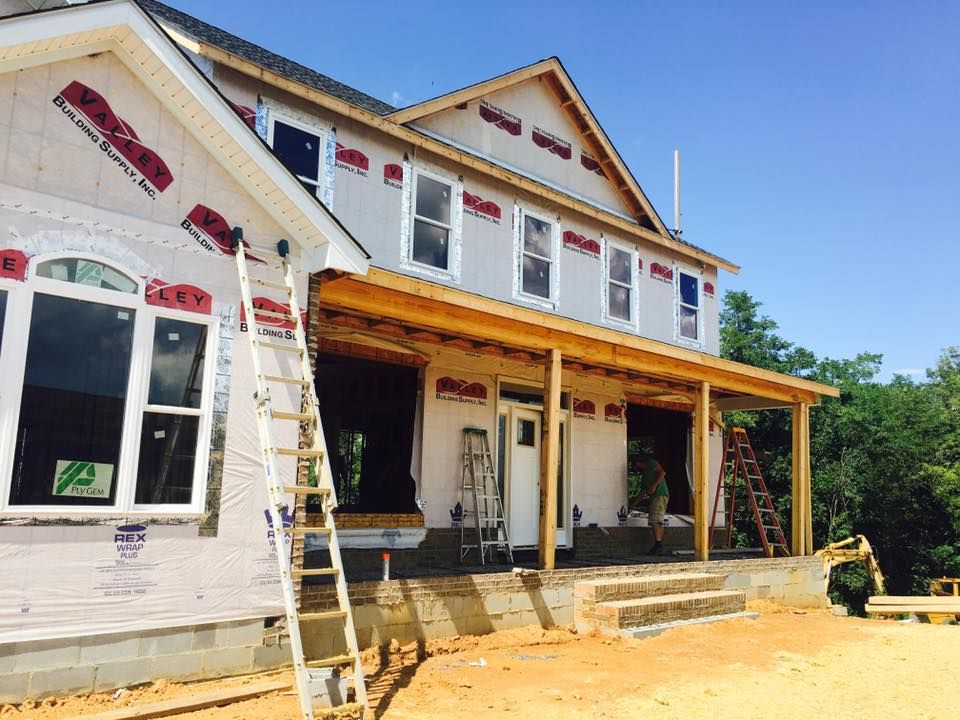 House under construction; two-story with porch, windows, wrapped in building paper, wooden framing, blue sky.