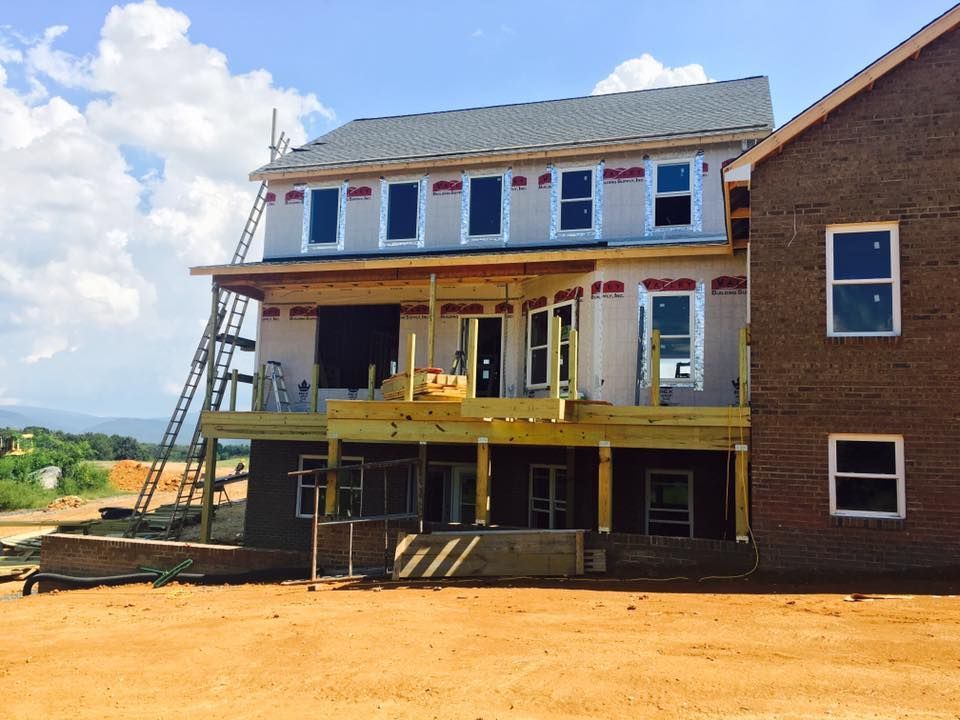 Construction of a two-story house with a wooden deck, against a cloudy blue sky.