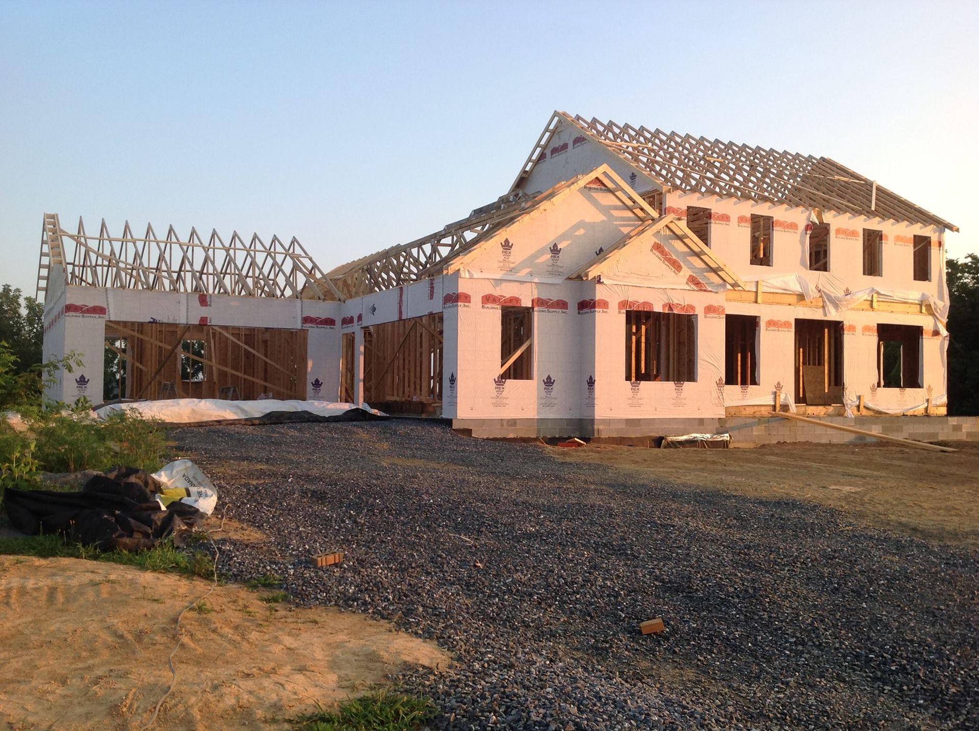 House under construction, wood frame, tarpaper, unfinished roof. Gravel and dirt in the foreground.