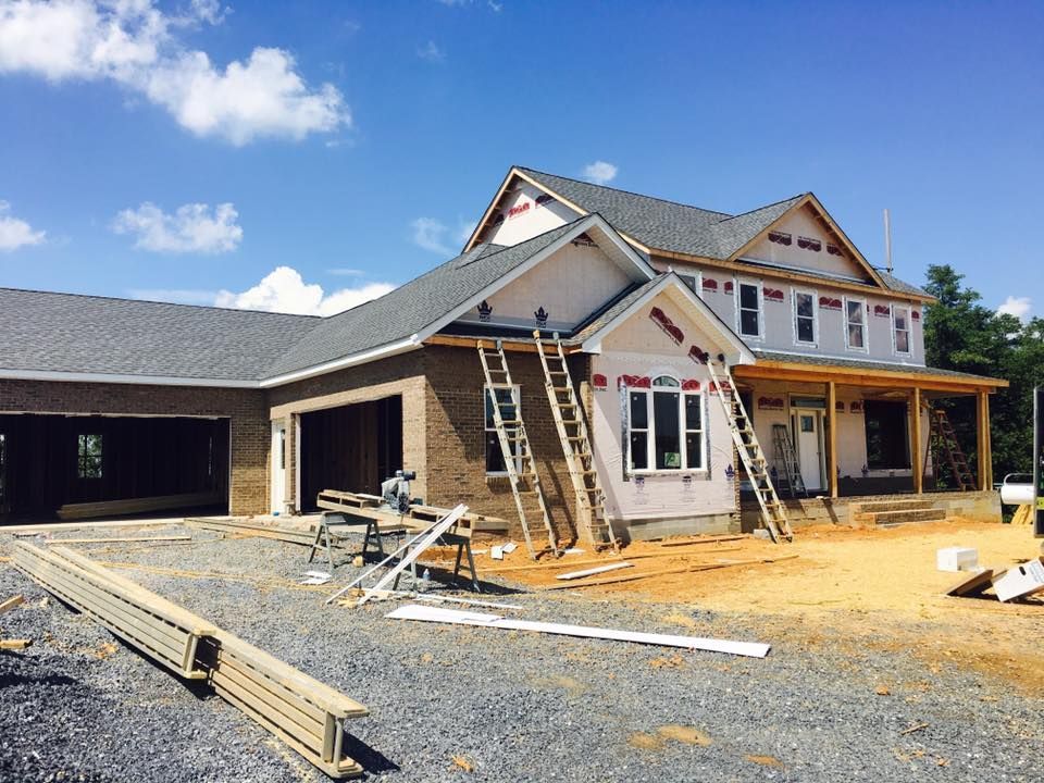 House under construction with brick facade, two-car garage, and ladders propped against the exterior.