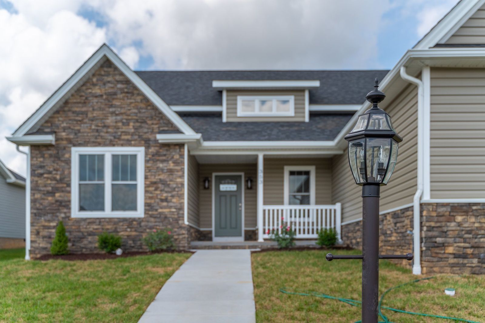 Stone and beige house with a grey roof and a paved walkway.