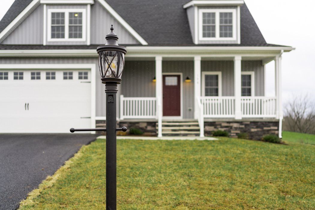 Gray house with porch, dormers, and a lamppost on the front lawn.