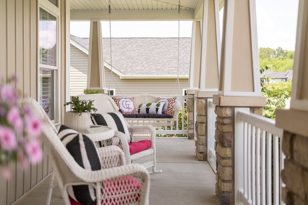 A porch with wicker furniture and a swing. Beige and white exterior, with colorful pillows.