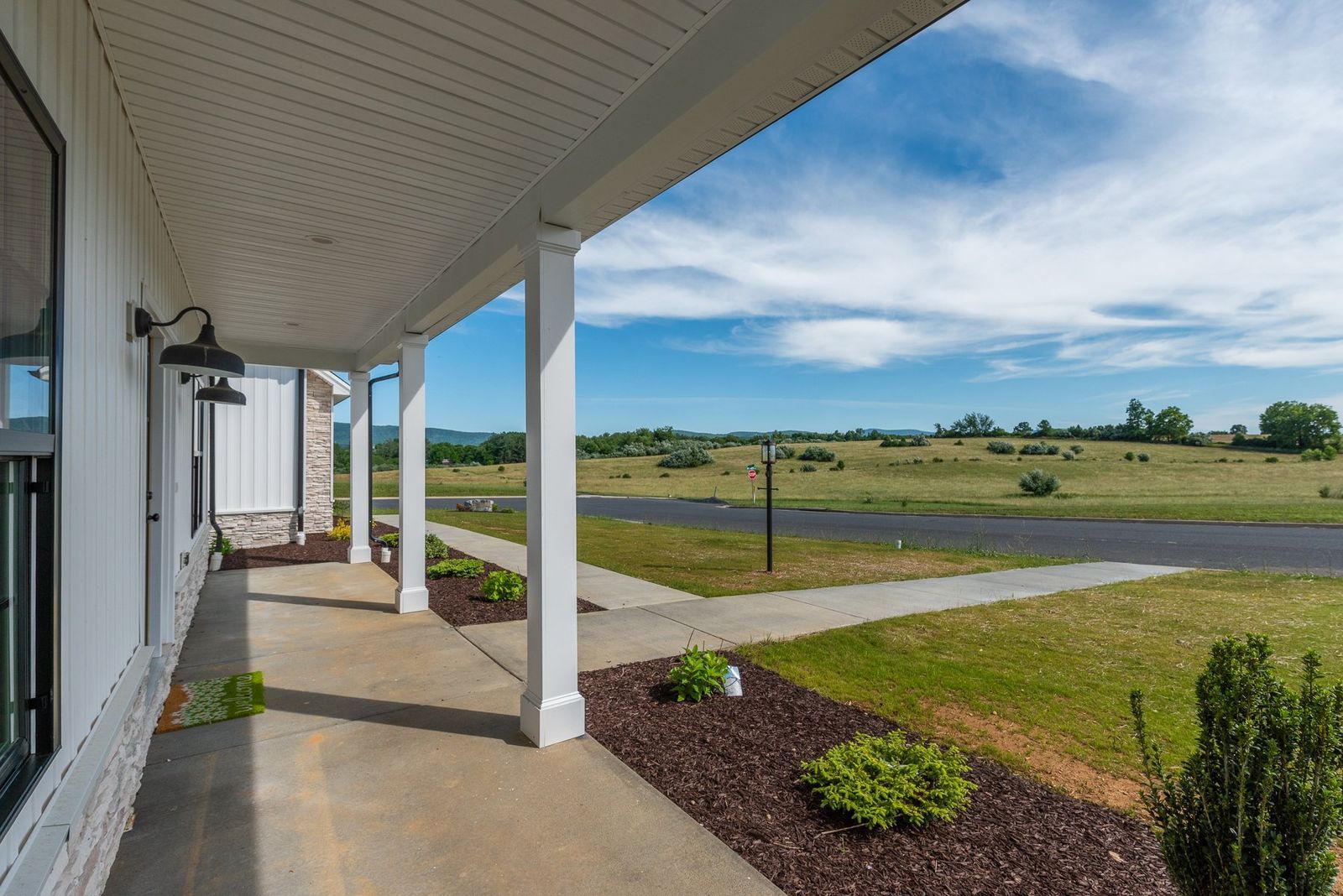Covered porch with white columns overlooking a grassy field under a blue sky.