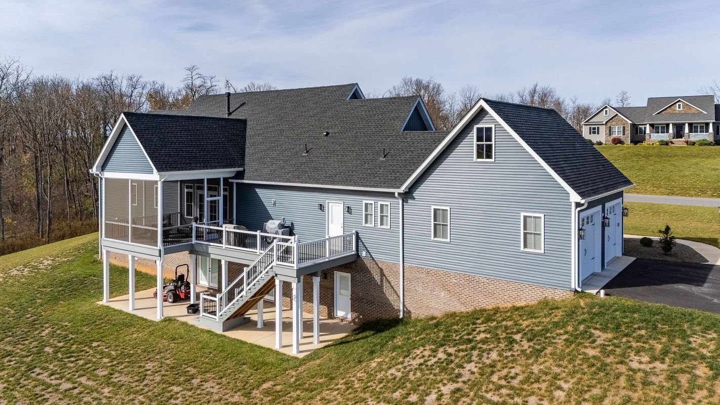 Blue house with screened porch, stairs, and garage on a grassy hillside.