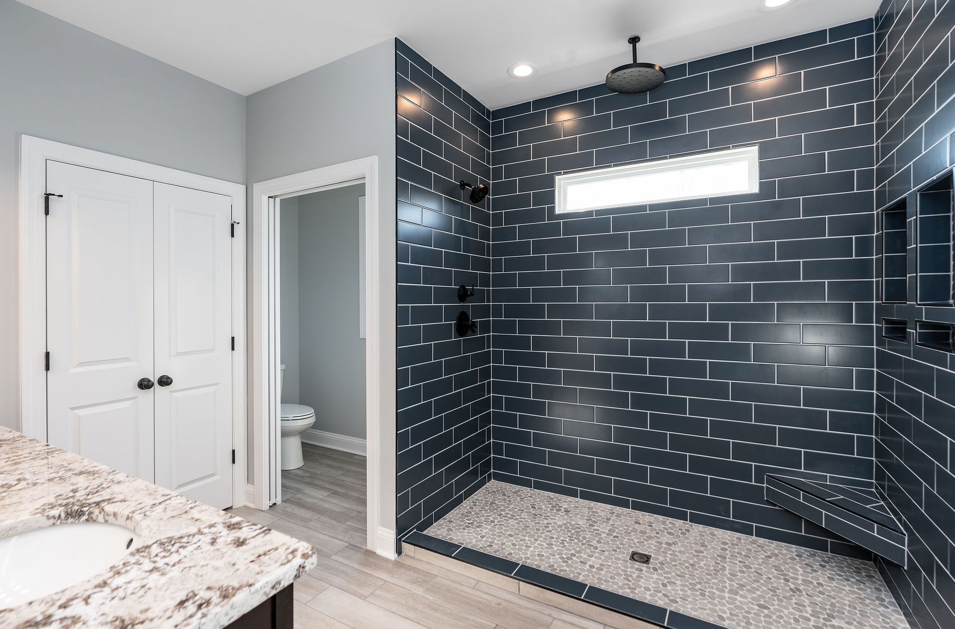 Modern bathroom with dark blue tiled shower, pebble floor, and granite countertop.