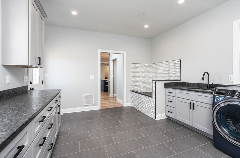 Laundry room with gray cabinets, countertop, and floor. Washer, sink, and dog wash station.