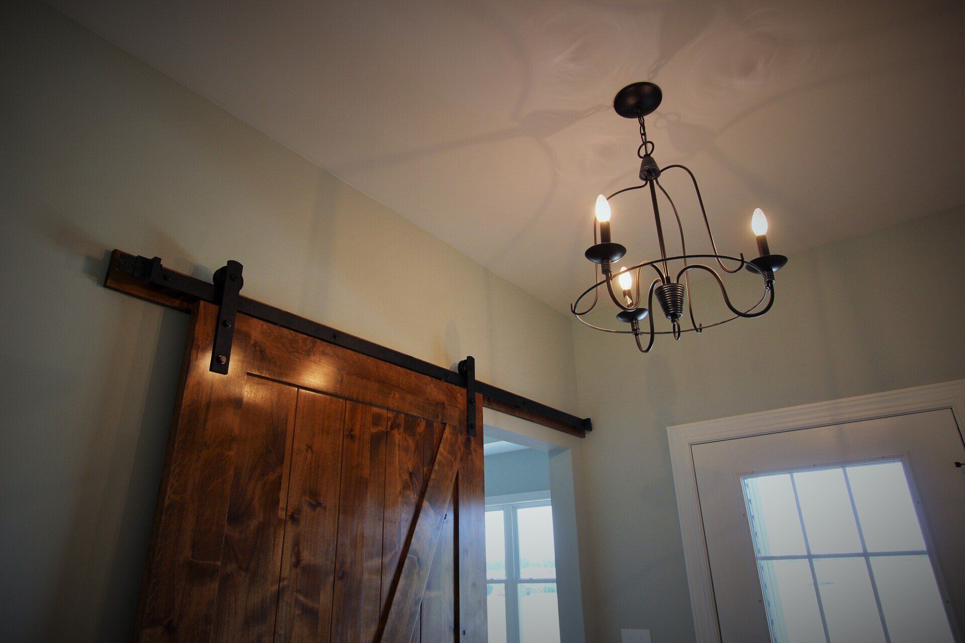 Barn door and chandelier in a room with light green walls.