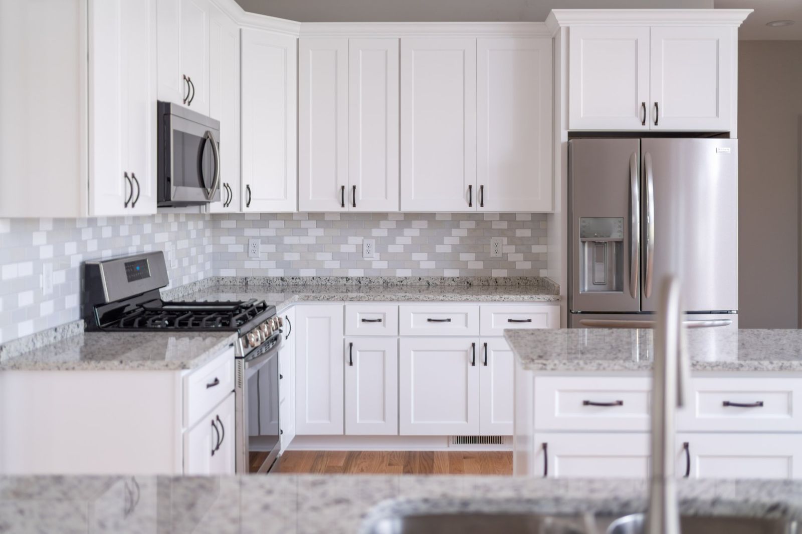White kitchen with white cabinets, stainless steel appliances, and granite countertops.