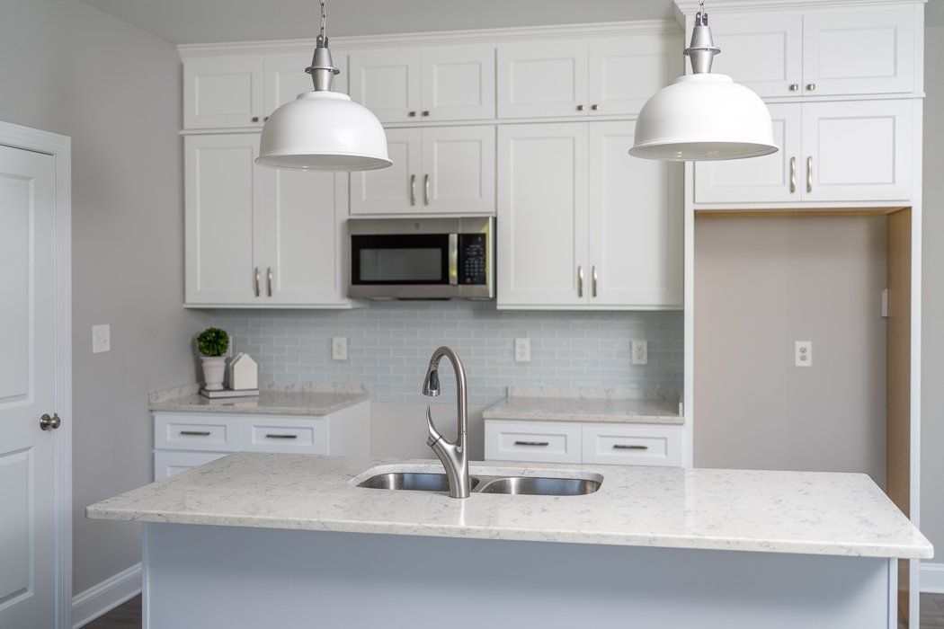 White kitchen with island, cabinets, microwave, and two pendant lights.