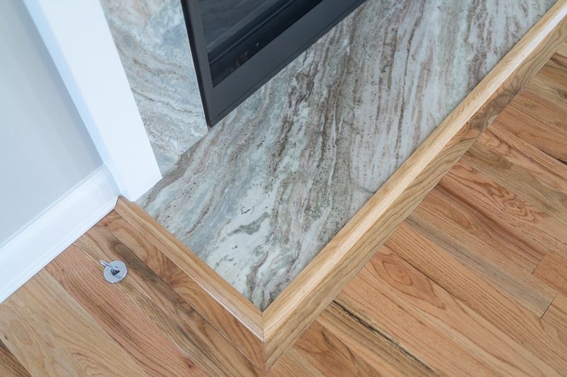 Wooden floor with trim meets a patterned stone fireplace surround.