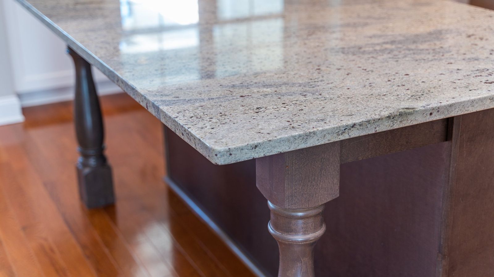 Granite countertop on a dark brown kitchen island with wood flooring, natural light.