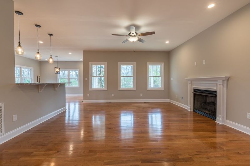 Spacious living room with hardwood floors, a fireplace, and three windows; neutral walls and pendant lights.