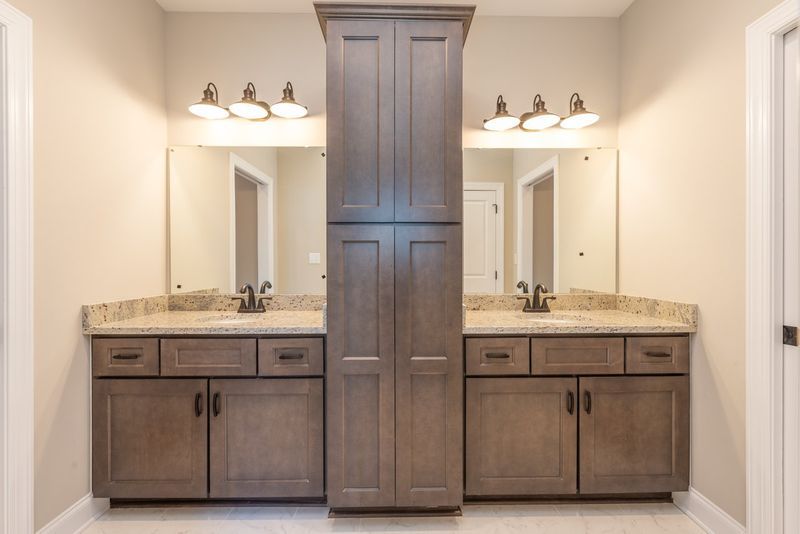 Bathroom with two vanities, mirrors, and a tall cabinet. Gray cabinets, beige countertops, and white walls.
