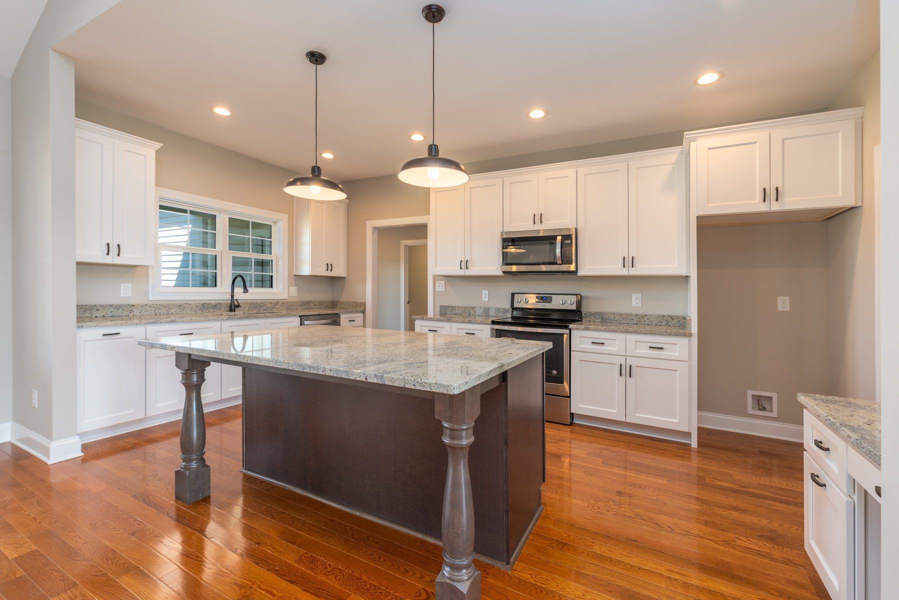 Kitchen with white cabinets, granite countertops, and a dark brown island with pendant lights.