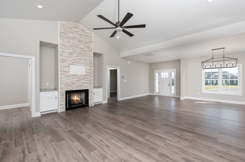 Spacious living room with fireplace, built-in shelves, and dark wood flooring. Light gray walls, vaulted ceiling.