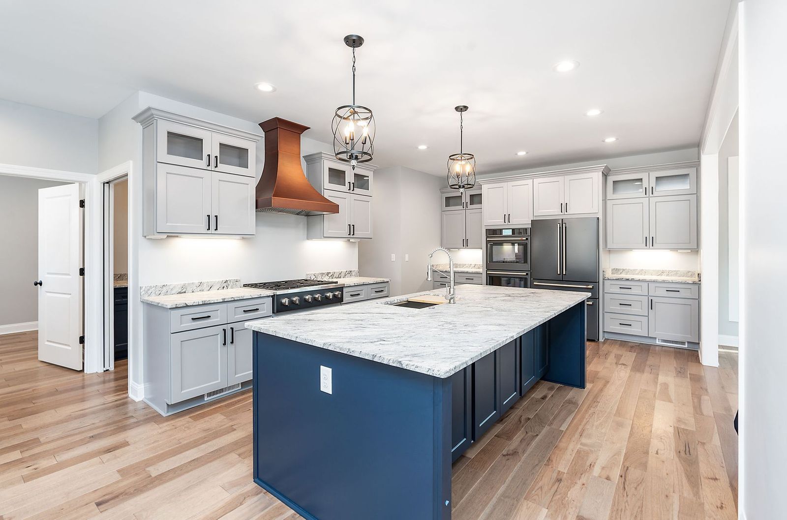 Modern kitchen with blue island, gray cabinets, wooden floors, and copper range hood.