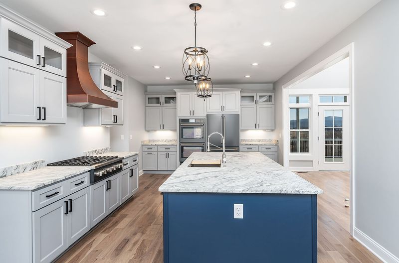 Modern kitchen with blue island, light grey cabinets, copper hood, and wood floors.