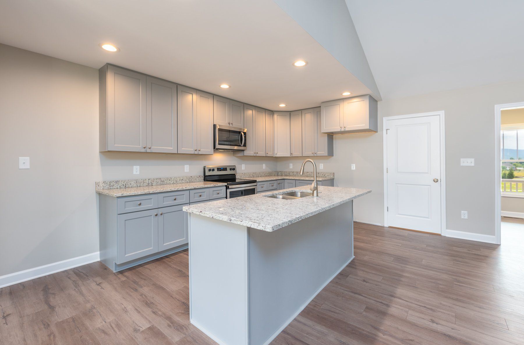 Kitchen with gray cabinets, granite countertops, island, stainless appliances, and wood-look flooring.
