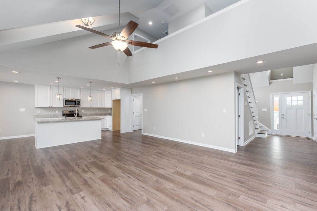 Bright, open living space with kitchen and loft area. Gray walls, wood-look flooring, white cabinetry.