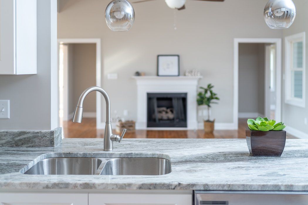 Kitchen sink and countertop in foreground, looking into a living room with fireplace and potted plant.