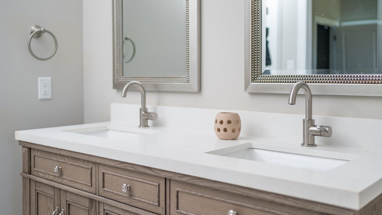 Bathroom with two sinks, two mirrors, light-colored countertop, and a wooden vanity with drawers.