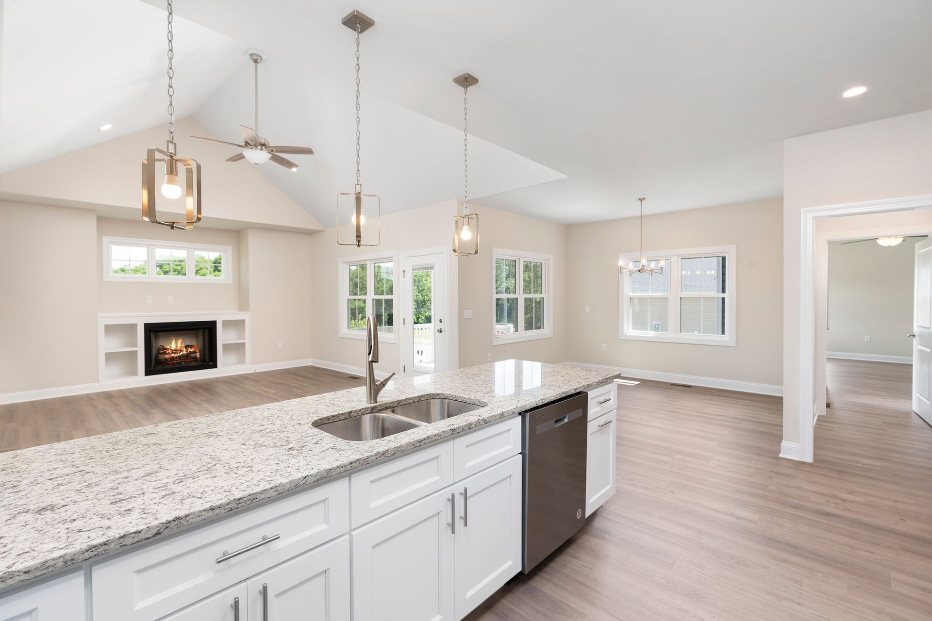 Open-concept kitchen with white cabinets, granite countertop island, stainless steel appliances, and a fireplace in the background.