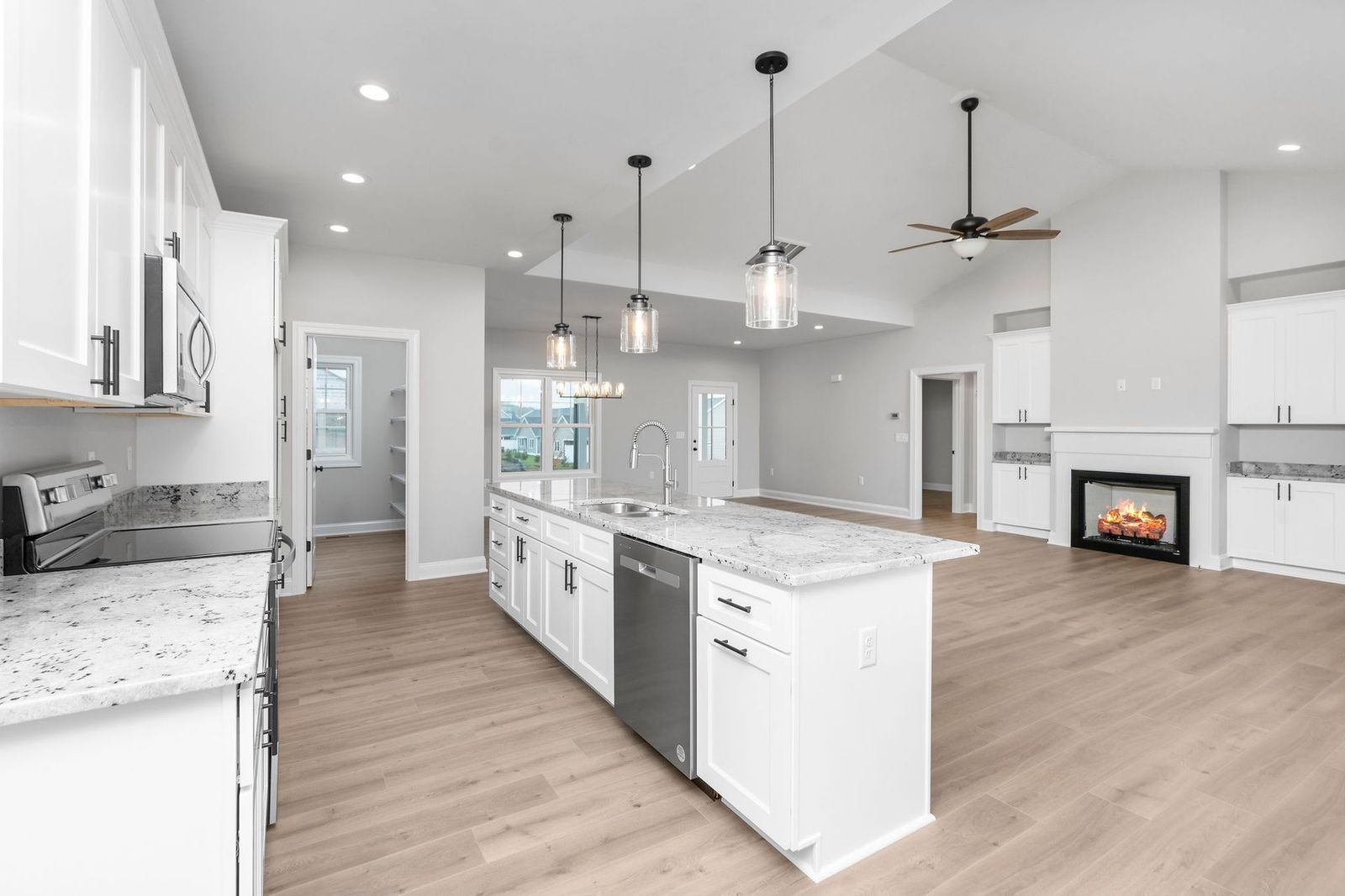 Bright, open kitchen with white cabinets, island, granite countertops, and fireplace in the background.