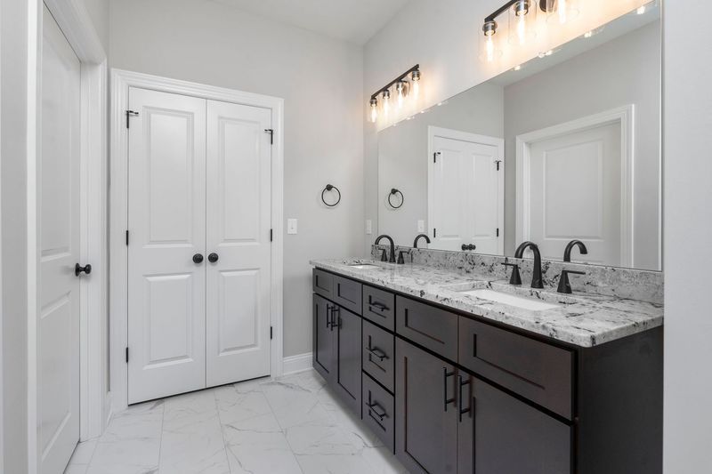 Bathroom with double sinks, dark wood vanity, large mirror, and white doors.
