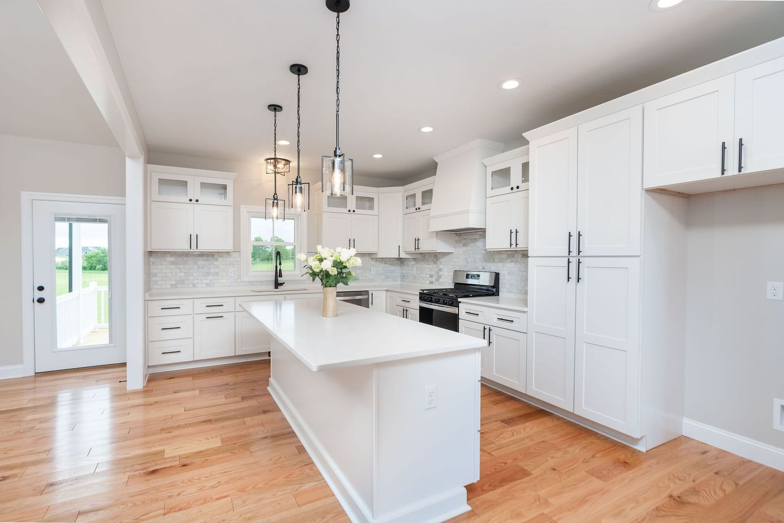 Bright, white kitchen with island, cabinets, and hardwood floors. Three hanging pendant lights over the island.
