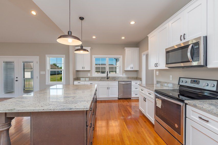 Bright kitchen with white cabinets, granite countertops, and stainless steel appliances. Island with dark base and wood floor.