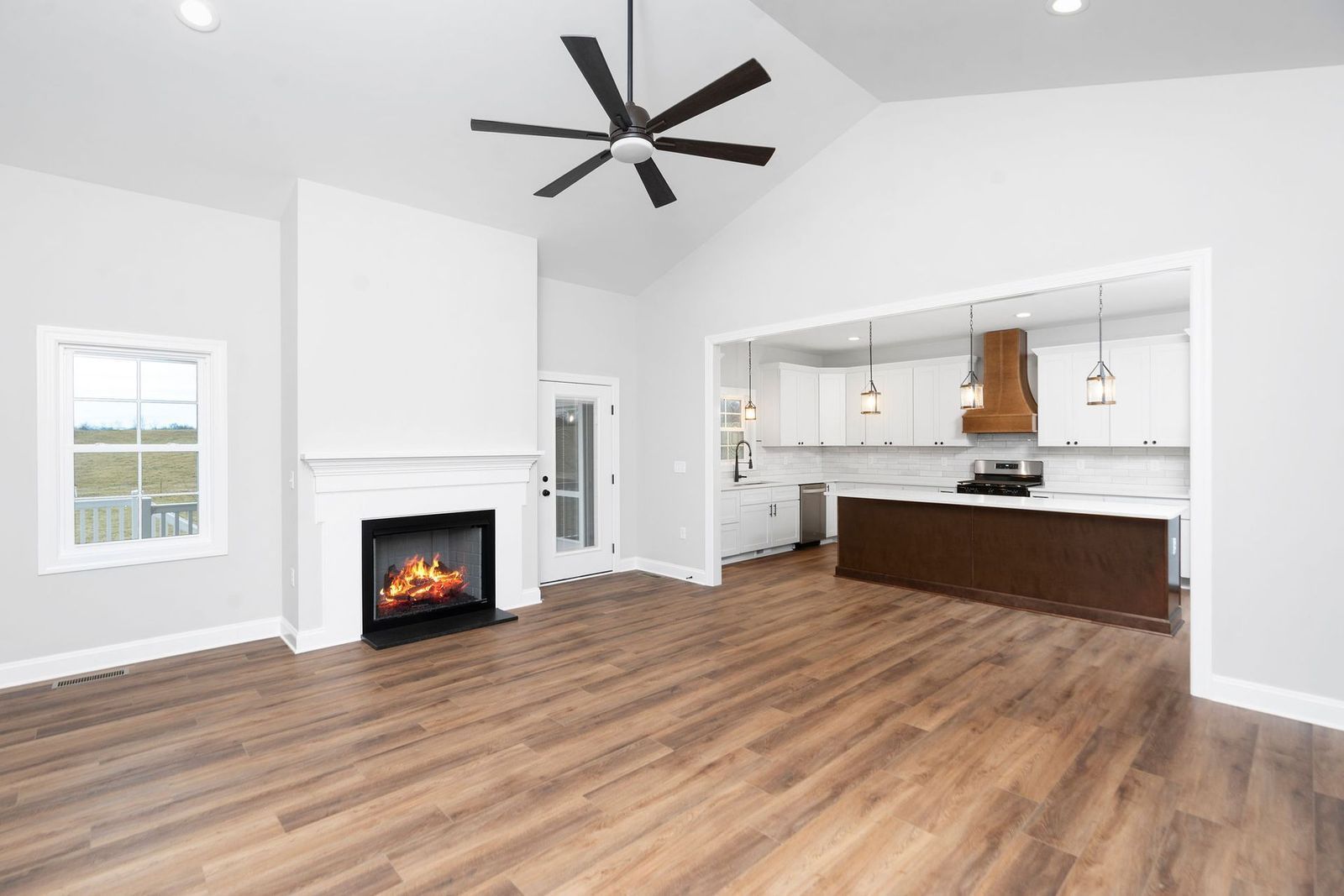 Spacious living room with fireplace, open to a kitchen, light walls, and wood flooring.