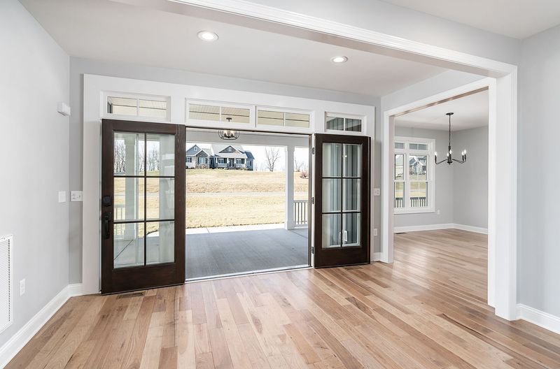 Interior with light wood floors, open doors leading to a porch and yard, and another doorway to an adjacent room.