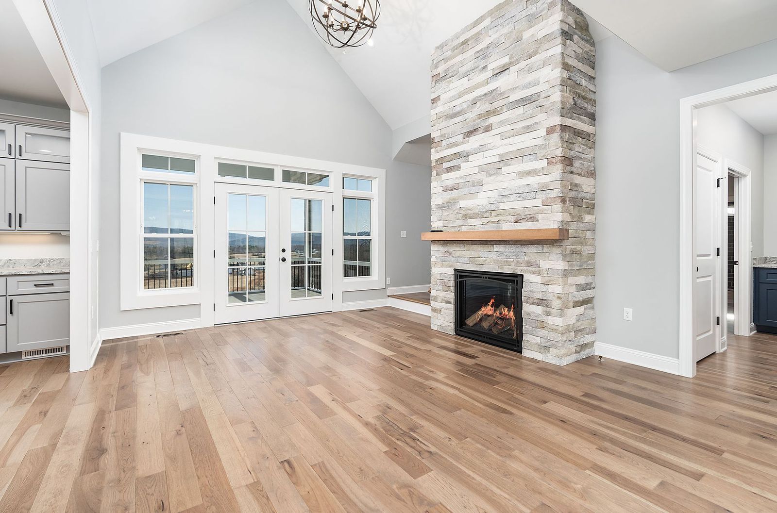 Spacious living room with hardwood floors, a stone fireplace, and French doors leading outside.