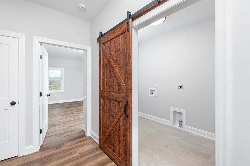Hallway with wooden sliding door to laundry room, and door to a room with window.