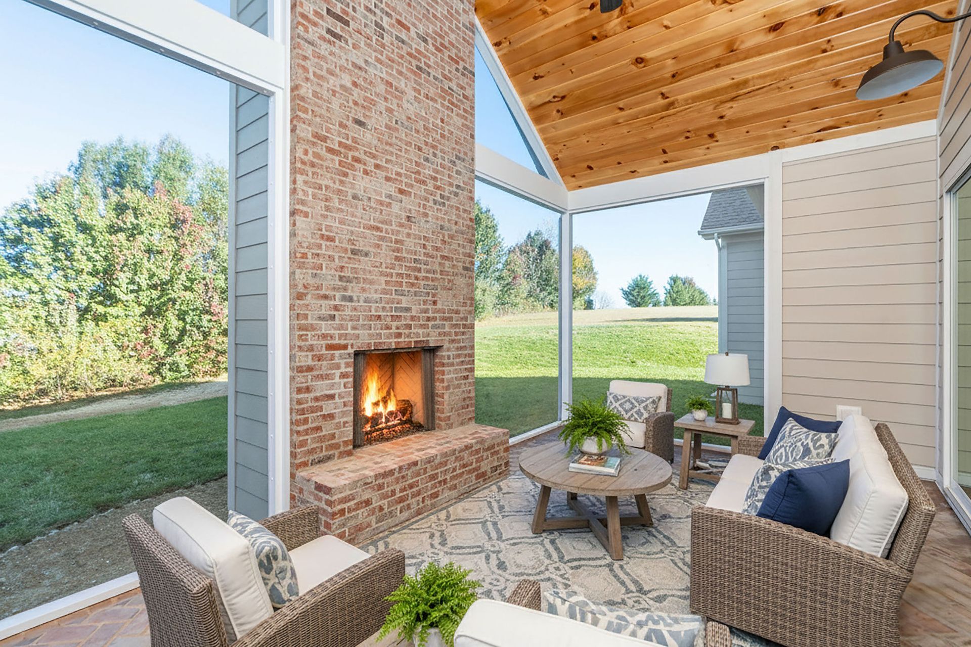 Screened porch with brick fireplace, seating, and view of green yard.