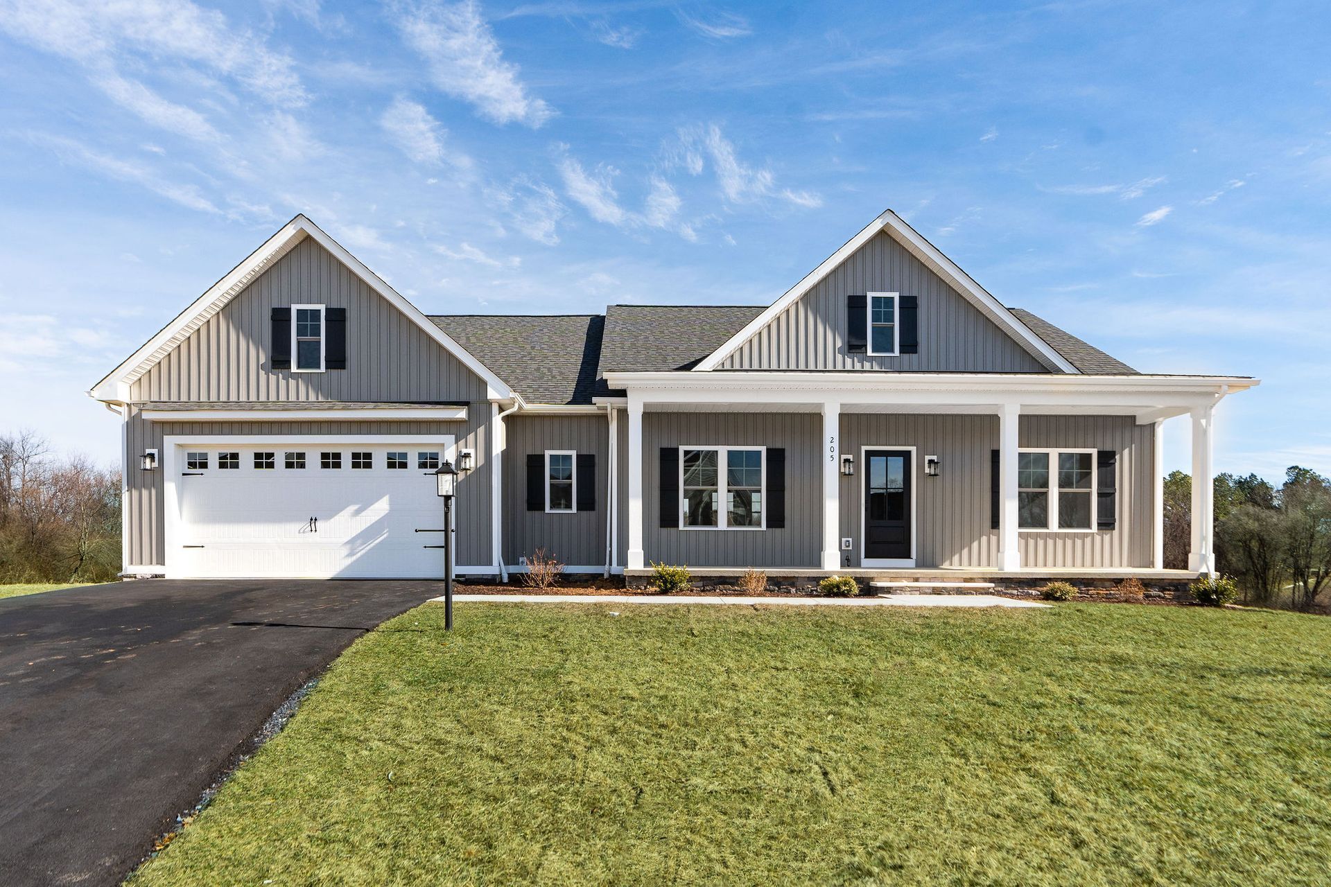 Gray house with a white garage door and front porch, set against a blue sky and green lawn.